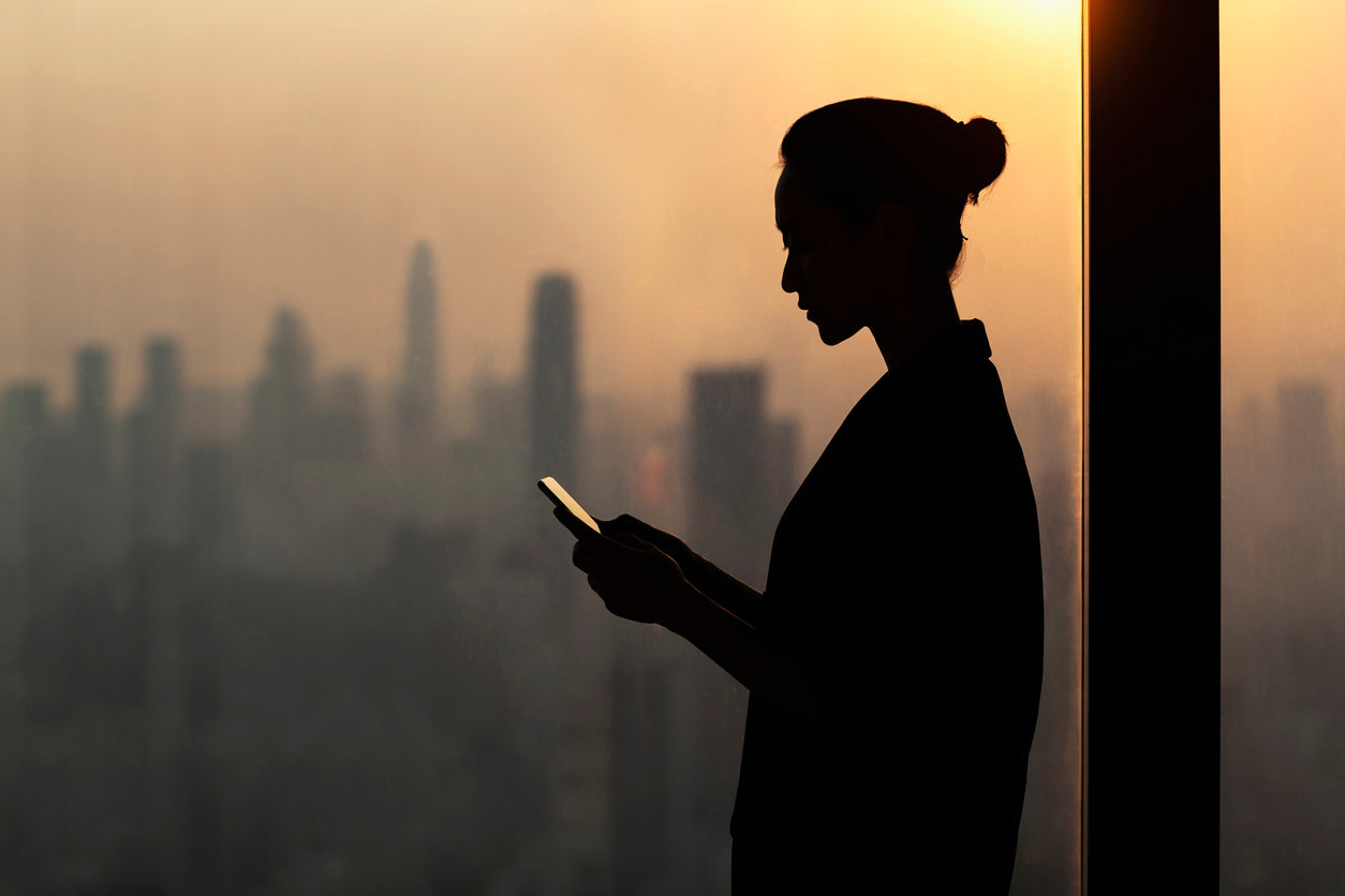 Femme tenant un téléphone devant une skyline urbaine, à contre-jour